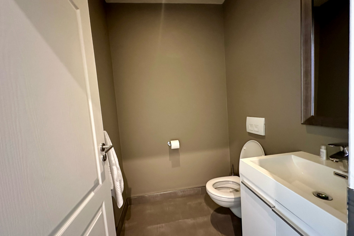 A clean and modern guest bathroom featuring a wall-mounted toilet, a sleek vanity with an integrated sink, and a neutral color palette.