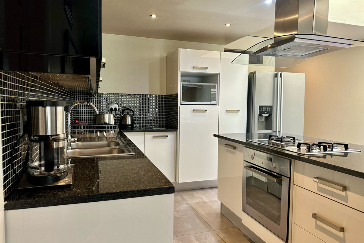 Modern kitchen featuring high-gloss cabinetry, granite countertops, a gas hob, built-in oven, and a stylish mosaic tile backsplash.