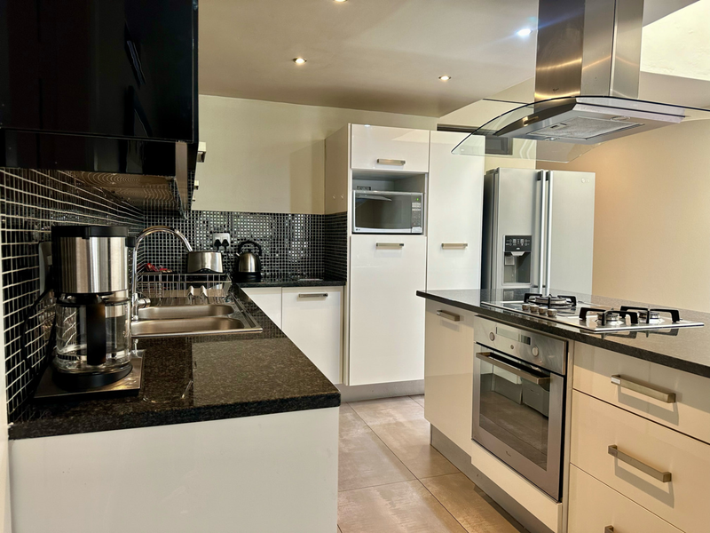 Modern kitchen featuring high-gloss cabinetry, granite countertops, a gas hob, built-in oven, and a stylish mosaic tile backsplash.