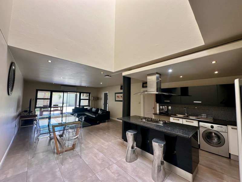 Spacious open-plan living and dining area featuring a modern kitchen with granite countertops, gas hob, integrated appliances, and a high-ceiling skylight.