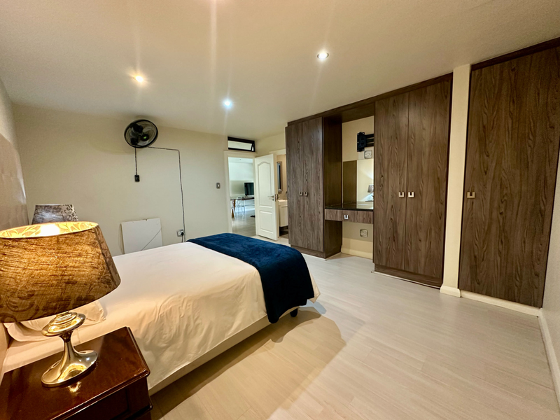 Spacious bedroom featuring extensive built-in wooden cabinetry, a dedicated vanity area, modern laminate flooring, and recessed ceiling lighting.