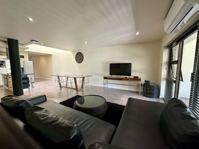 Spacious open-plan living and dining area featuring tiled floors, recessed lighting, and a wall-mounted air conditioning unit with access to an outdoor space.