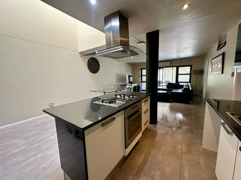 Modern open-plan living area featuring a sleek kitchen island with granite countertops, built-in oven, gas hob, and stainless steel extractor fan.