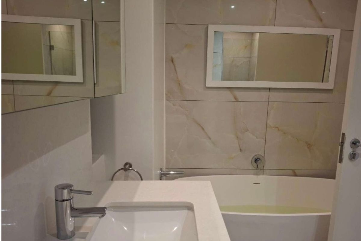 Modern bathroom featuring a sleek freestanding bathtub, marble-look wall tiling, and a contemporary vanity with a mirrored cabinet.