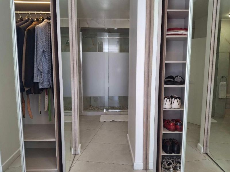 A bedroom featuring built-in cupboards with mirrored doors and an en-suite bathroom with a glass shower enclosure.