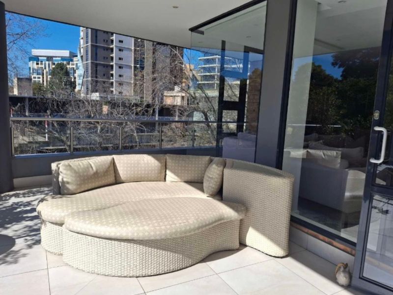 A modern covered balcony featuring tiled flooring, a glass balustrade, and large sliding doors, offering an open-air space with urban views.