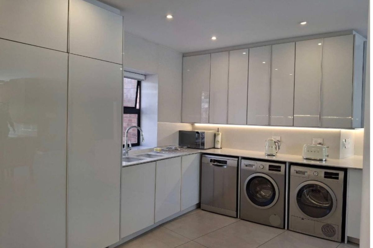 Modern kitchen featuring high-gloss white cabinetry, integrated appliances, under-cabinet lighting, and sleek tiled flooring in a clean, contemporary layout.