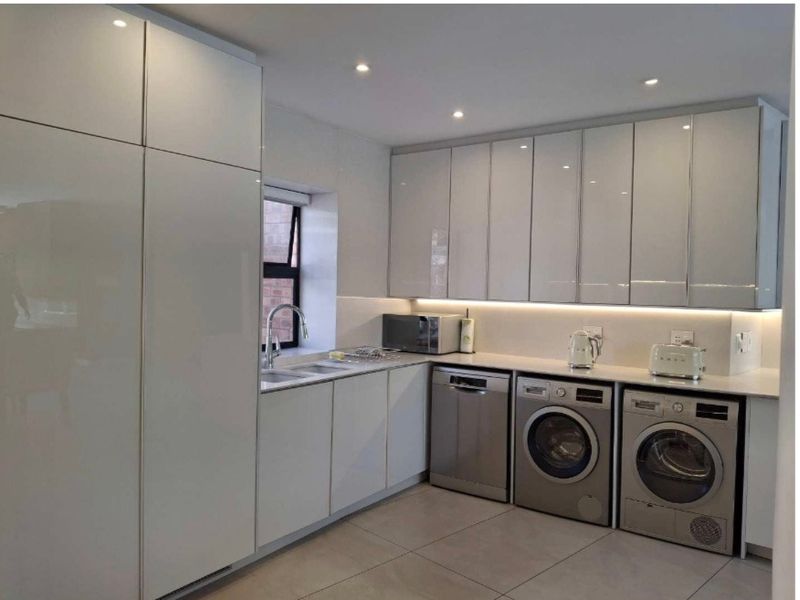 Modern kitchen featuring high-gloss white cabinetry, integrated appliances, under-cabinet lighting, and sleek tiled flooring in a clean, contemporary layout.