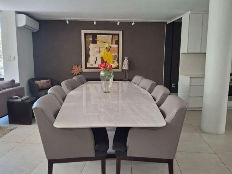 An open-plan dining and living area featuring tiled floors, track lighting, a split-system air conditioner, and integrated kitchen cabinetry.