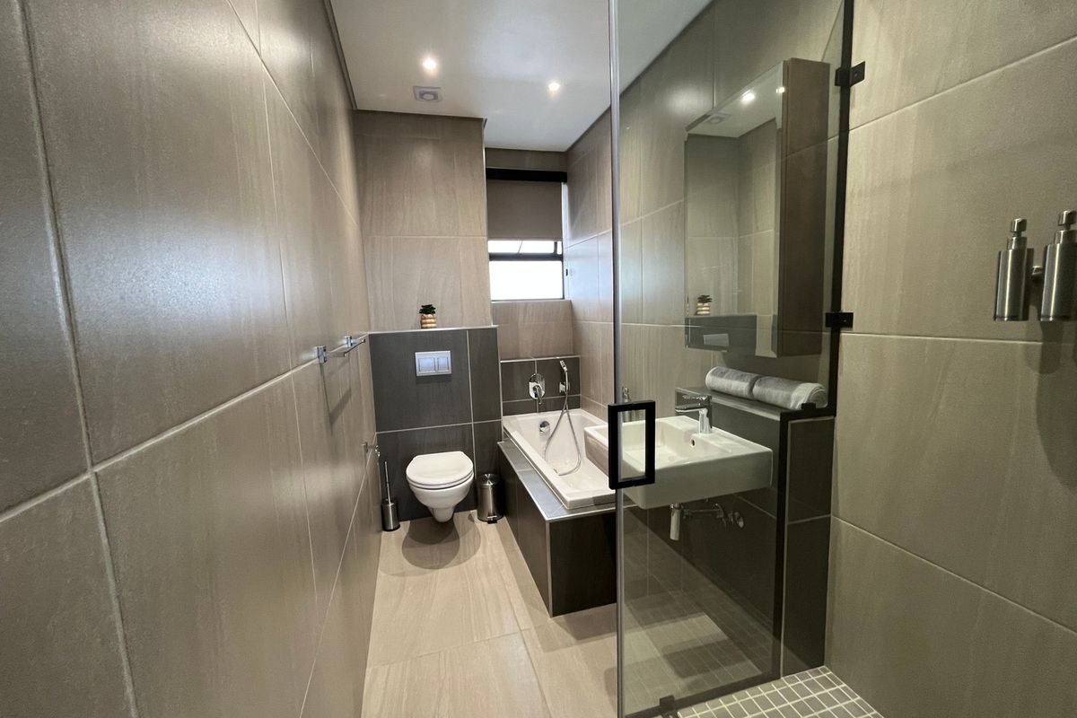 Modern bathroom featuring large format wall tiles, a wall-mounted toilet, a built-in bathtub, and a separate shower area with a glass screen.