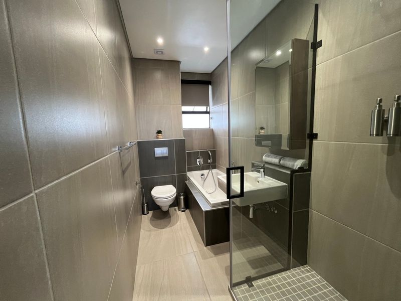 Modern bathroom featuring large format wall tiles, a wall-mounted toilet, a built-in bathtub, and a separate shower area with a glass screen.