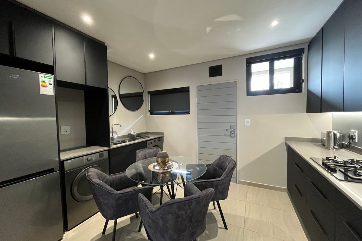 Modern open-plan kitchen and dining area featuring sleek dark cabinetry, stone countertops, gas hob, and integrated laundry facilities with contemporary finishes.