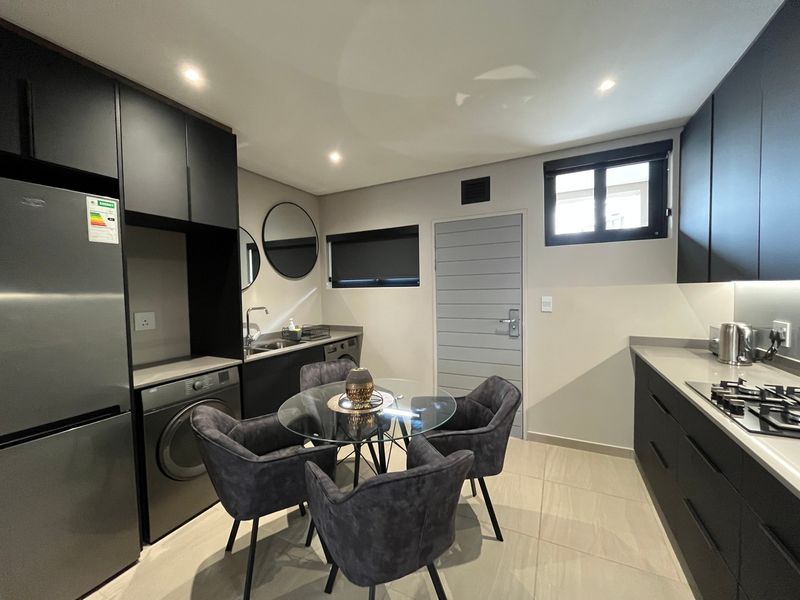 Modern open-plan kitchen and dining area featuring sleek dark cabinetry, stone countertops, gas hob, and integrated laundry facilities with contemporary finishes.