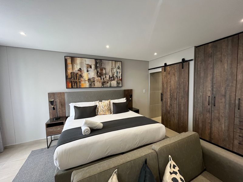 Modern bedroom featuring built-in wooden cabinetry, a sliding barn door leading to an en-suite, and recessed ceiling lighting.