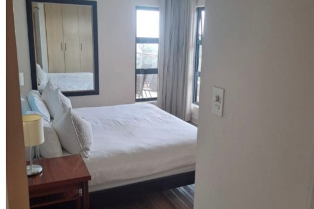 A well-lit bedroom featuring laminate flooring, built-in cupboards, and large windows that provide natural light and access to an outdoor area.
