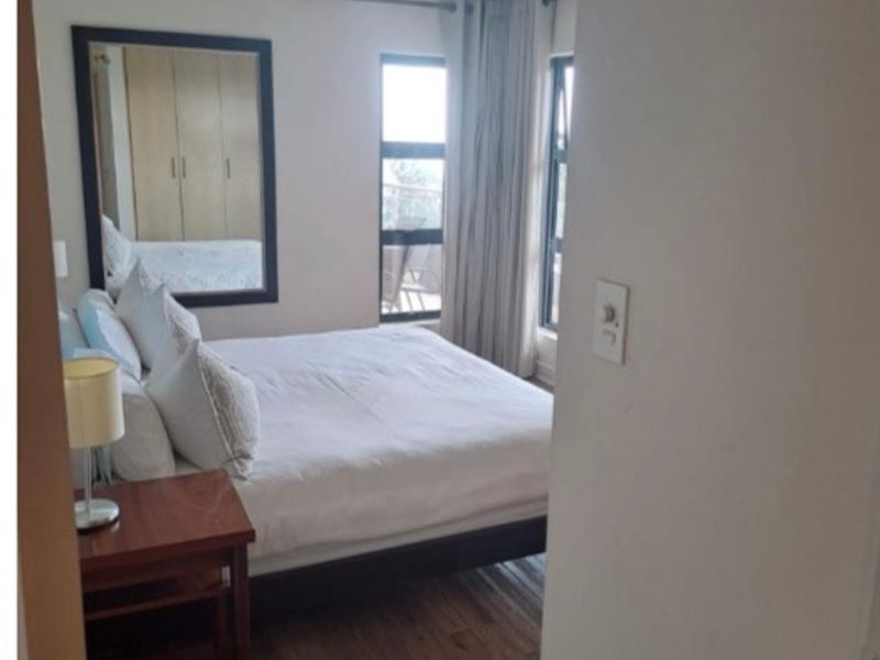 A well-lit bedroom featuring laminate flooring, built-in cupboards, and large windows that provide natural light and access to an outdoor area.