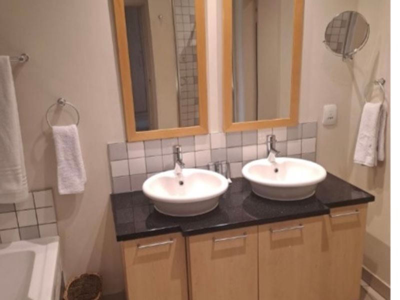 A well-maintained bathroom featuring a double vanity with vessel sinks, granite countertops, built-in cabinetry, and a bathtub with tiled flooring.