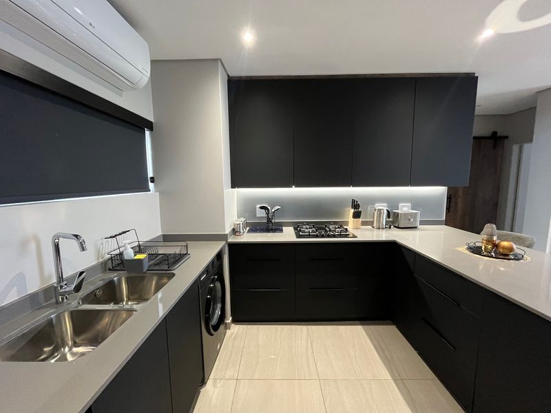 Modern kitchen featuring sleek matte black cabinetry, stone countertops, integrated appliances, gas hob, and under-cabinet lighting in a contemporary open-plan layout.