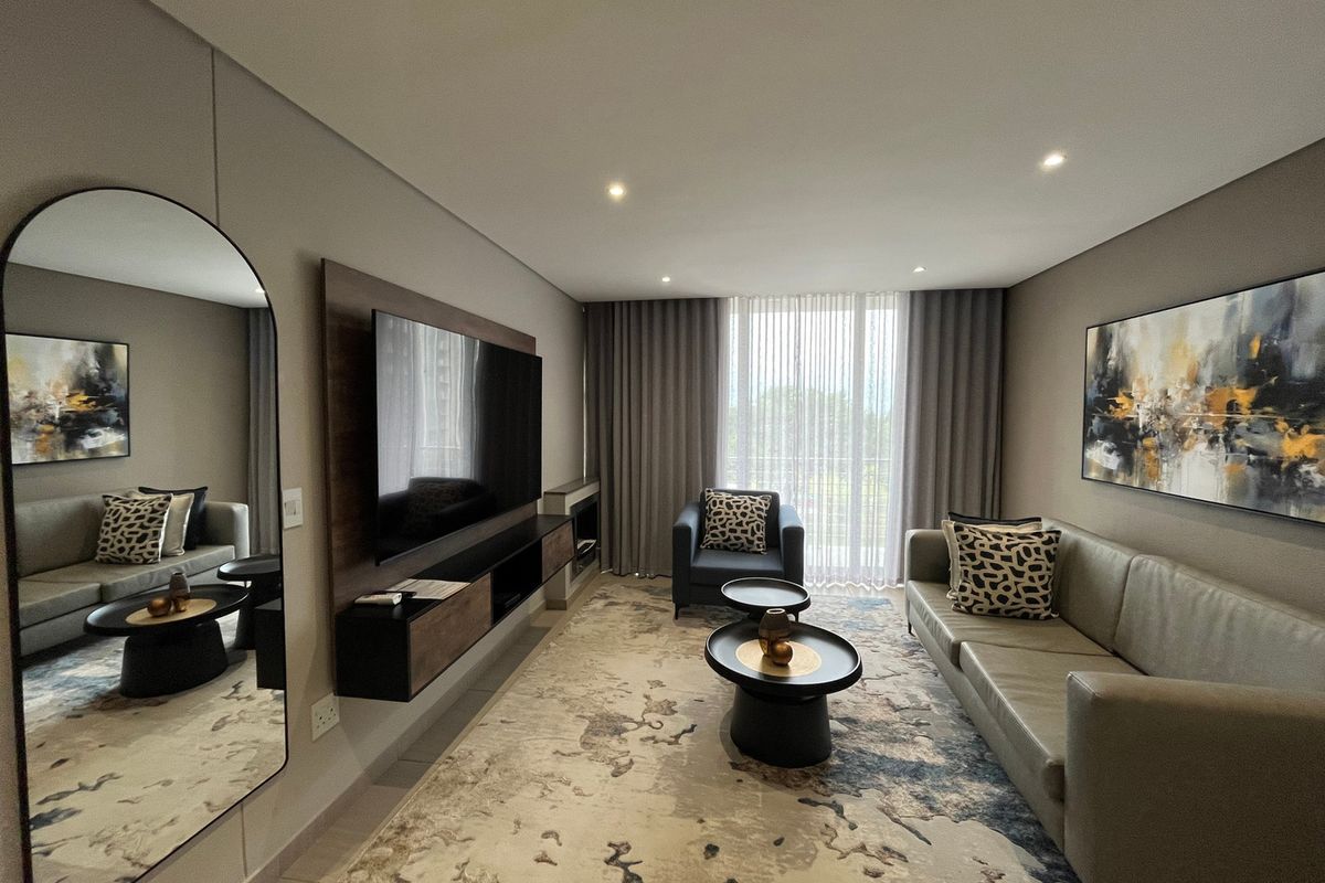 Modern living room featuring a built-in media console, recessed downlighting, and large windows with floor-to-ceiling curtains, creating a bright and contemporary atmosphere.