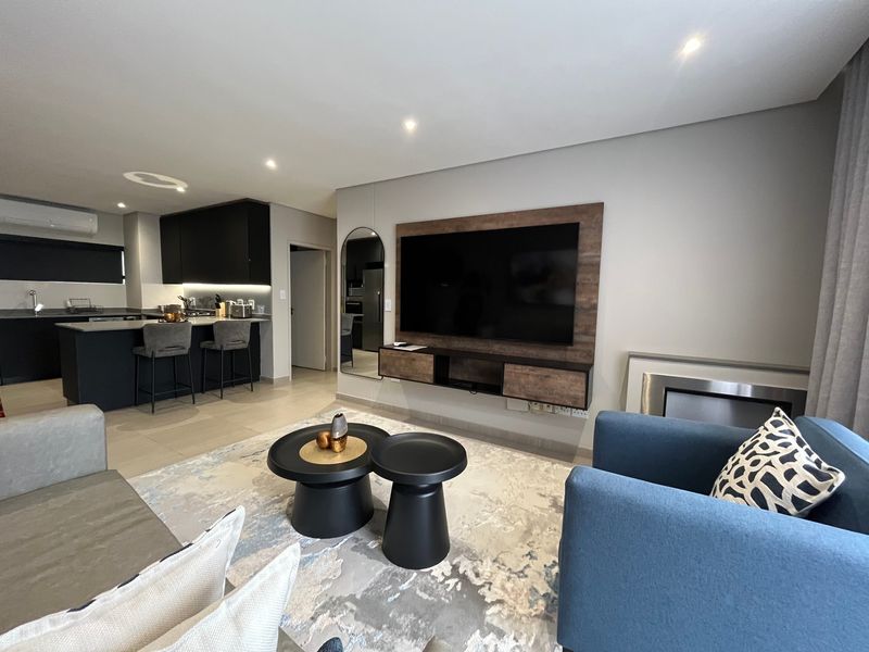 Modern open-plan living area featuring a sleek kitchen with island, recessed lighting, and a custom wall-mounted media console in a contemporary apartment setting.