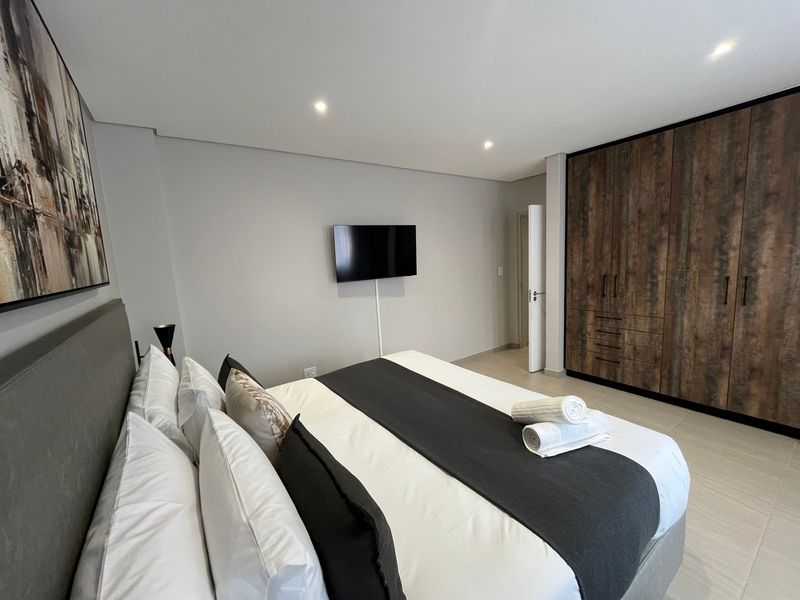 Modern bedroom featuring neutral tones, tiled flooring, recessed downlighting, and extensive built-in wooden cabinetry for storage.