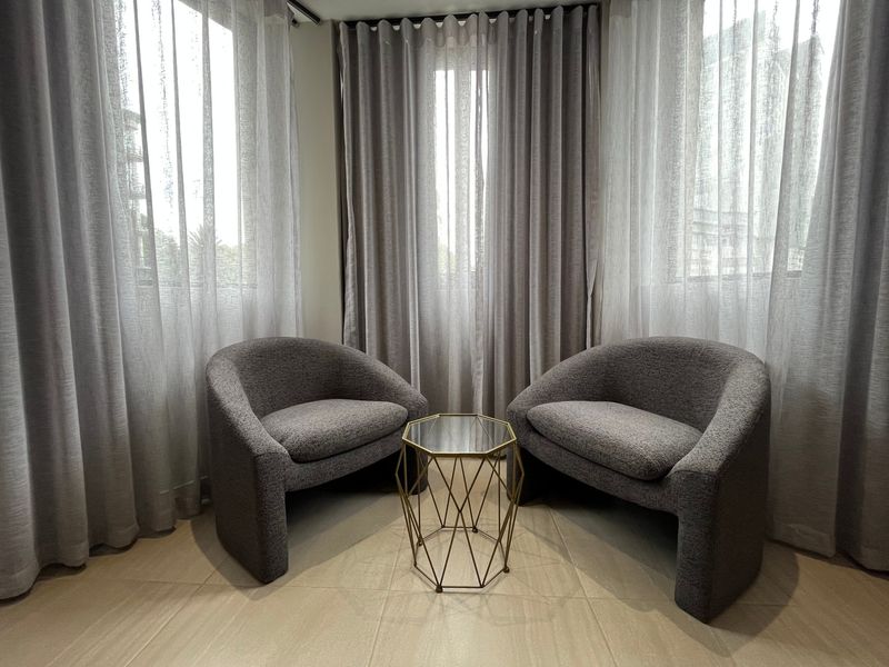 A bright living area featuring neutral tiled flooring and floor-to-ceiling curtains, creating a comfortable and well-lit space.