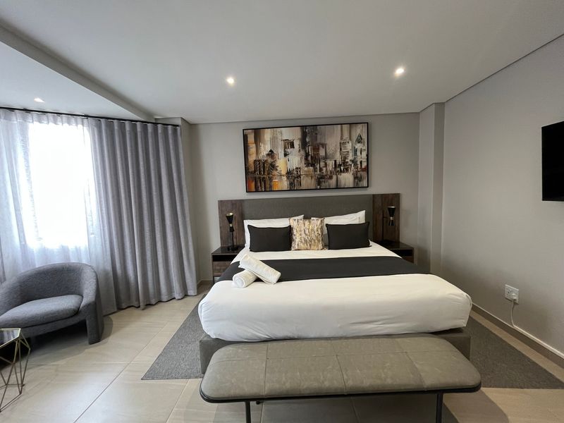 A well-maintained bedroom featuring neutral tiled flooring, recessed ceiling lighting, and integrated curtain tracks, offering a clean and modern living space.