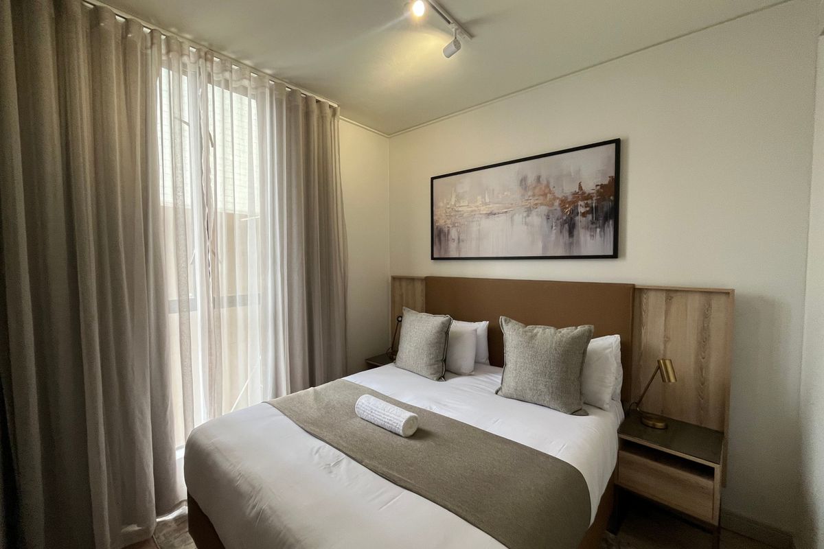 A well-maintained bedroom featuring a built-in headboard with integrated bedside tables and modern track lighting.