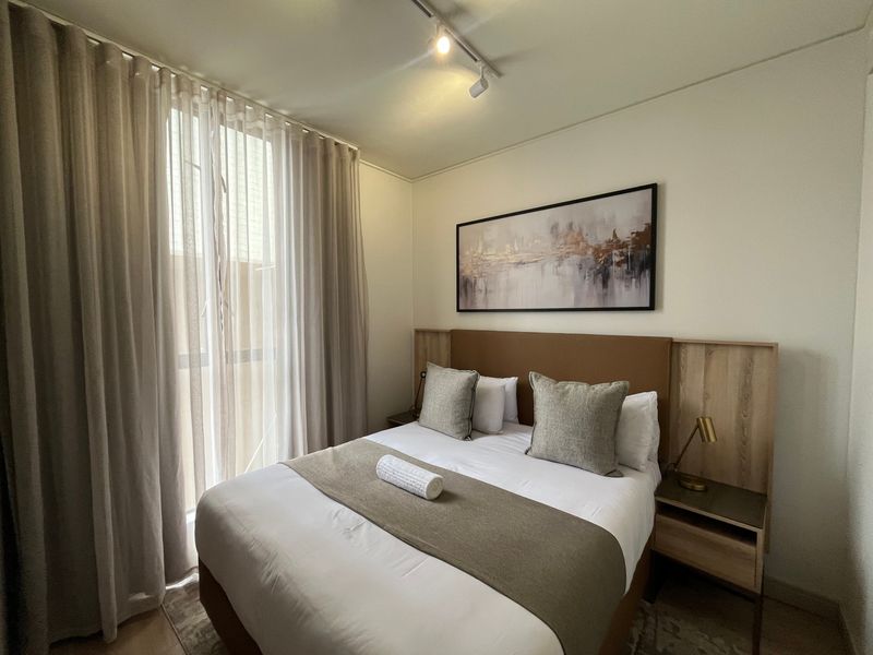 A well-maintained bedroom featuring a built-in headboard with integrated bedside tables and modern track lighting.