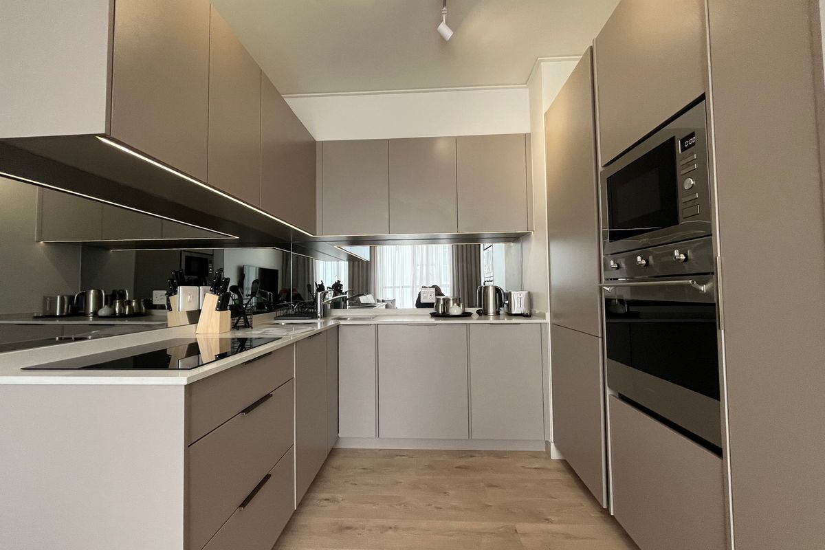 Modern, well-appointed kitchen featuring sleek handleless cabinetry, integrated appliances, stone countertops, and a stylish mirrored splashback with under-cabinet lighting.