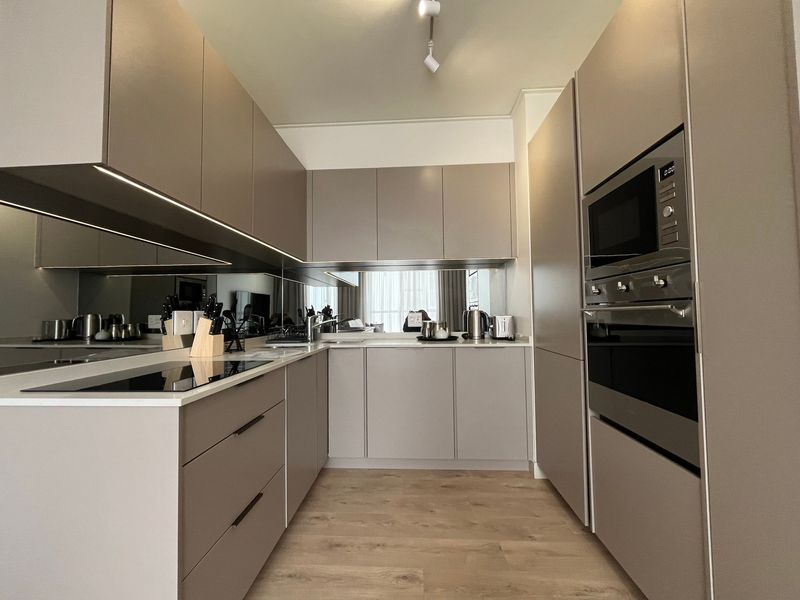 Modern, well-appointed kitchen featuring sleek handleless cabinetry, integrated appliances, stone countertops, and a stylish mirrored splashback with under-cabinet lighting.