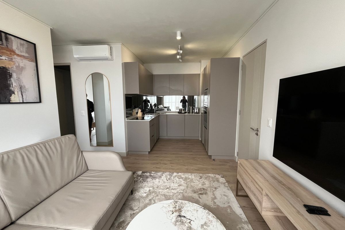 Modern open-plan living area featuring a sleek kitchen with integrated appliances, neutral cabinetry, and light wood-look flooring throughout the space.