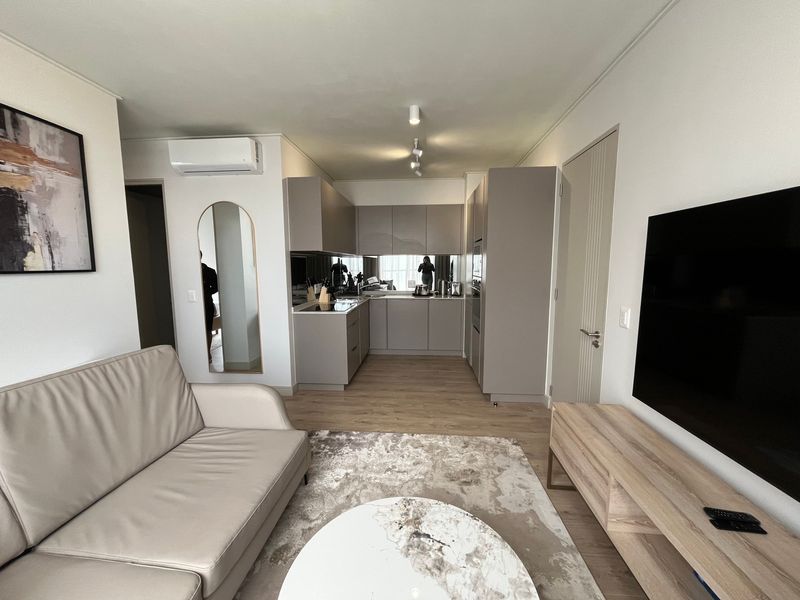 Modern open-plan living area featuring a sleek kitchen with integrated appliances, neutral cabinetry, and light wood-look flooring throughout the space.