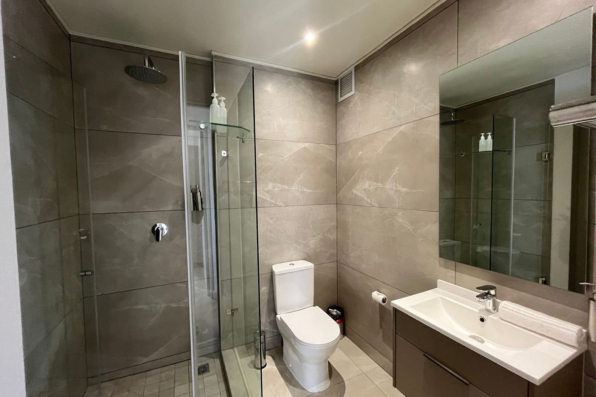 Modern bathroom featuring large-format neutral wall tiles, a glass-enclosed walk-in shower with rain head, wall-mounted toilet, and a sleek vanity with integrated basin.