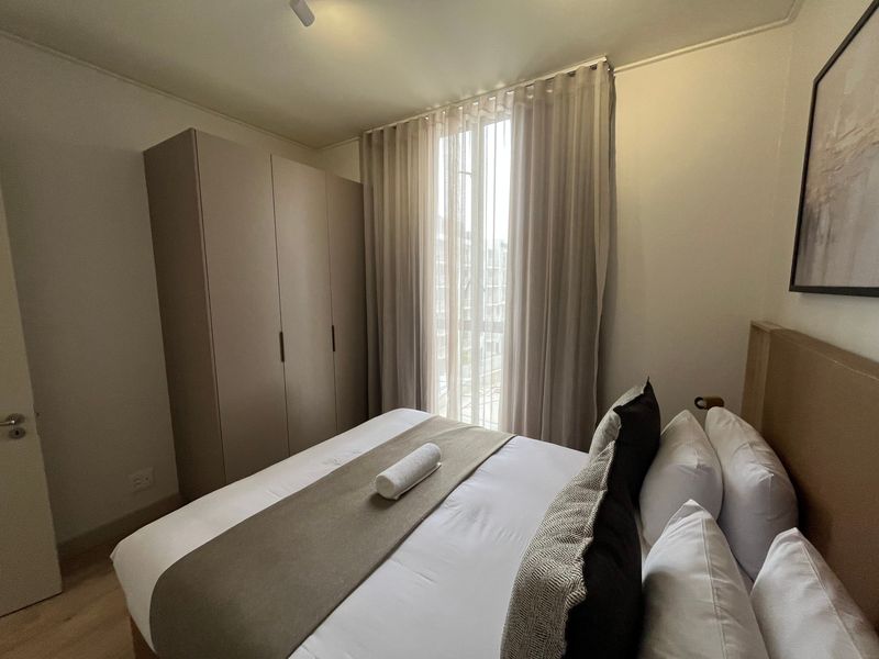 A well-maintained bedroom featuring neutral tones, built-in wardrobe storage, and floor-to-ceiling curtains allowing natural light.