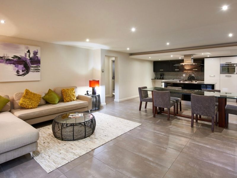 Spacious open-plan living and dining area featuring modern tiled floors, recessed lighting, and a sleek, well-equipped kitchen with built-in appliances.