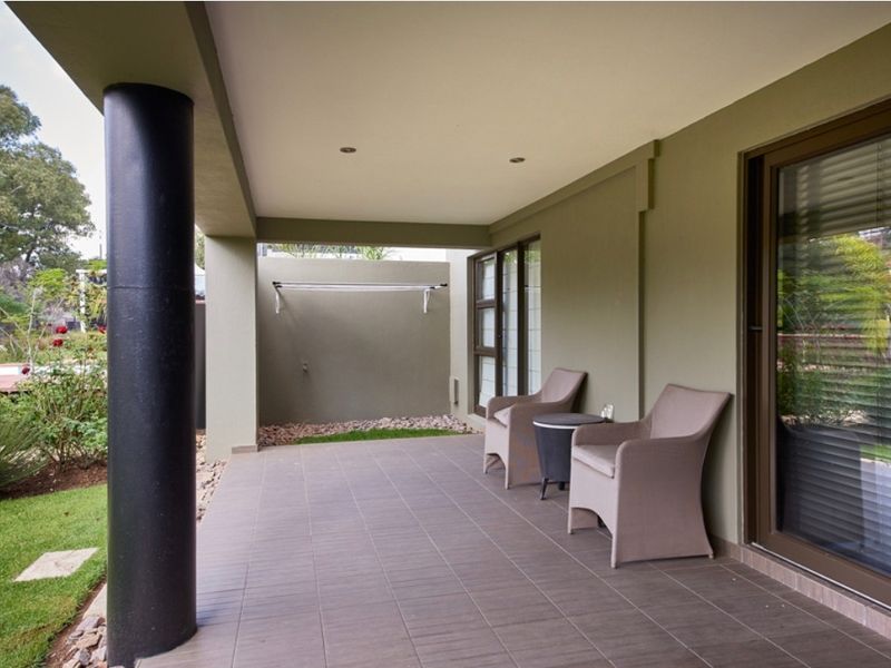 A covered outdoor patio featuring tiled flooring, recessed lighting, and direct access to the garden through sliding glass doors.