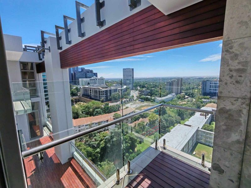 A modern balcony featuring timber decking, a sleek glass balustrade with stainless steel handrails, and expansive urban views.