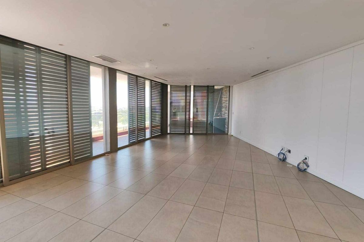 A spacious, empty living area featuring large format floor tiles, recessed lighting, ducted air conditioning, and floor-to-ceiling sliding doors with external metal shutters.