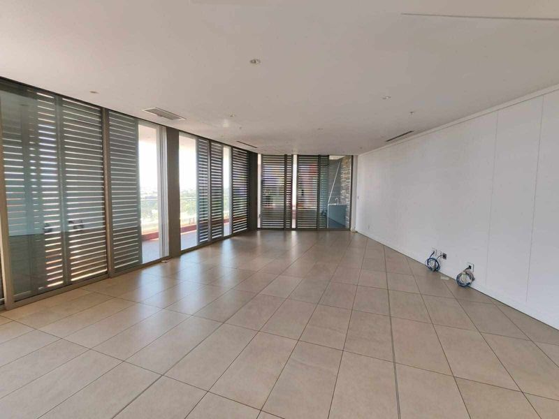 A spacious, empty living area featuring large format floor tiles, recessed lighting, ducted air conditioning, and floor-to-ceiling sliding doors with external metal shutters.