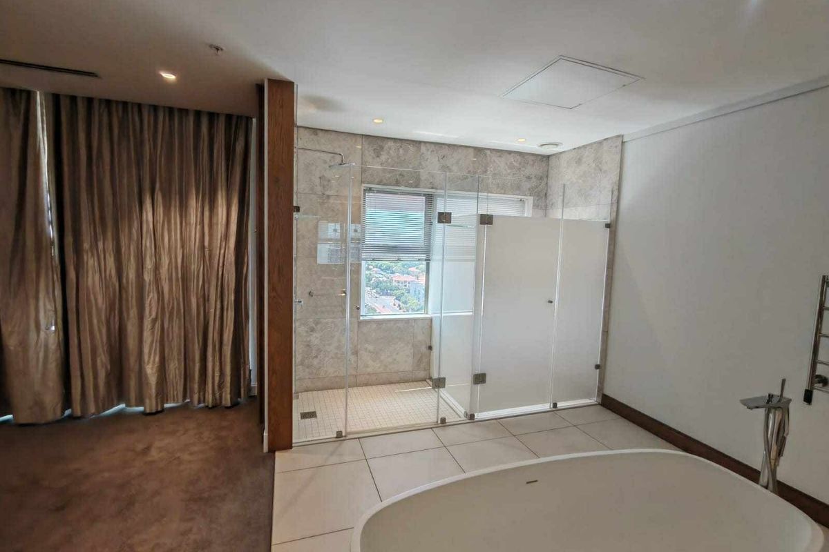 Modern open-plan bathroom featuring a freestanding bathtub, glass-enclosed shower with stone wall cladding, and high-quality tiled finishes.