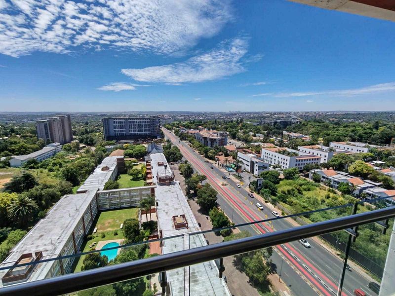 Elevated panoramic urban view captured from a balcony featuring a modern glass balustrade and metal handrail.