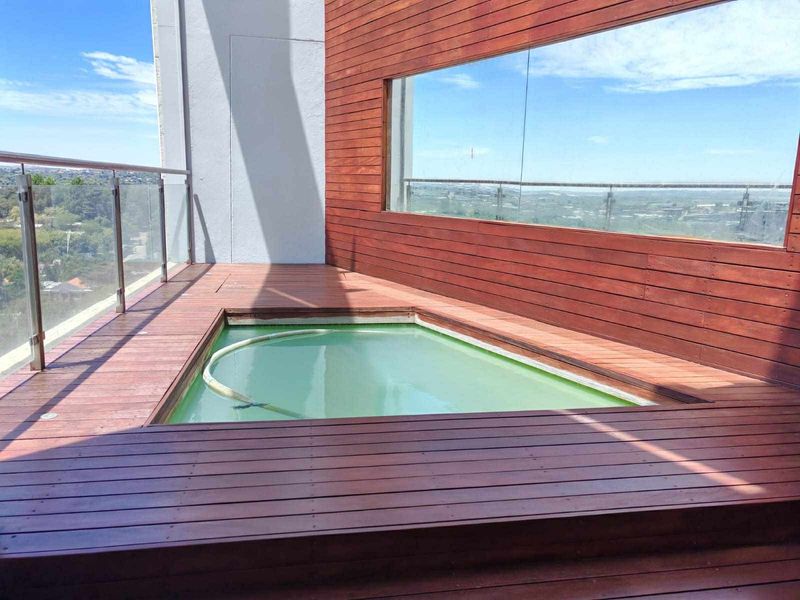 A private balcony plunge pool featuring timber decking, glass balustrades, and wood-paneled walls with expansive elevated views.