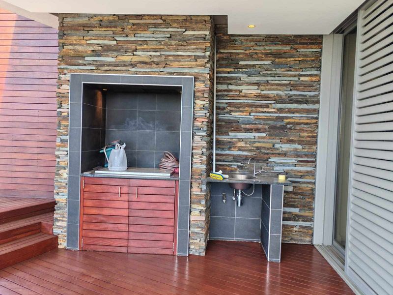 Covered patio area featuring a built-in braai, stone-clad feature wall, integrated sink, and timber decking, perfect for outdoor entertaining.