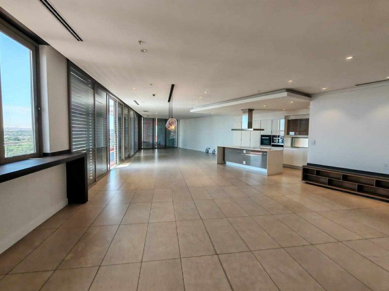 Spacious open-plan living and kitchen area featuring modern cabinetry, a central island, tiled flooring, and large sliding glass doors leading to a balcony.