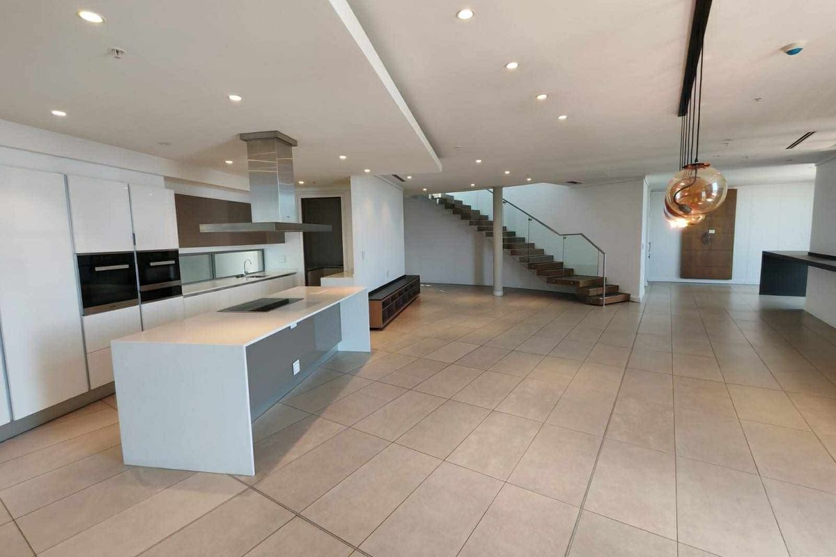 Spacious open-plan living area featuring a modern kitchen with a central island, sleek cabinetry, and a striking staircase with glass balustrades.