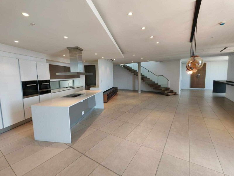Spacious open-plan living area featuring a modern kitchen with a central island, sleek cabinetry, and a striking staircase with glass balustrades.