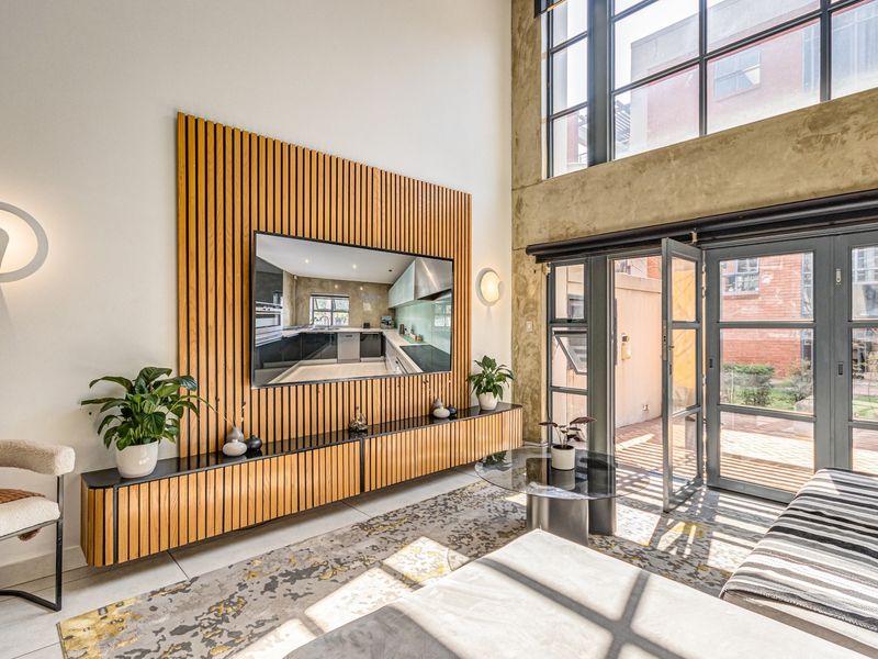 Modern double-volume living room featuring a timber slat feature wall, built-in cabinetry, and large steel-framed glass doors opening to an outdoor area.