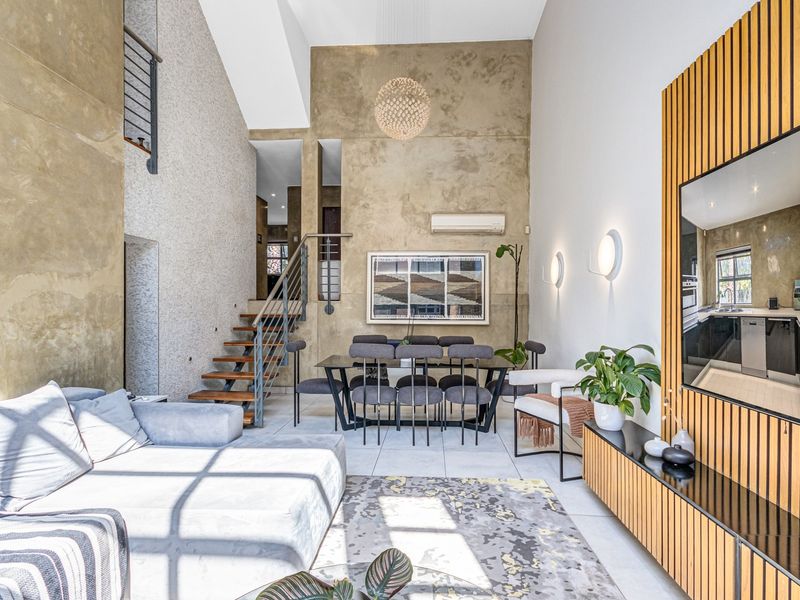 Spacious open-plan living and dining area featuring double-height ceilings, a modern staircase, tiled flooring, and integrated wall-mounted lighting.