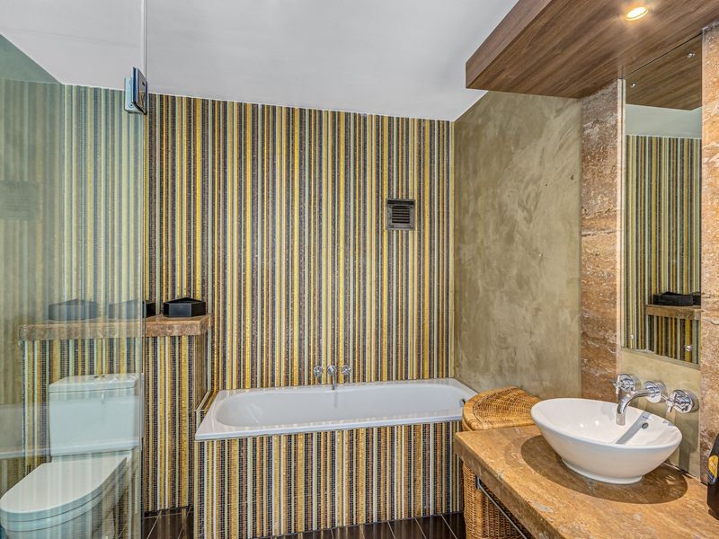 Modern bathroom featuring a built-in bathtub, stone vanity with a vessel sink, glass shower enclosure, and decorative mosaic wall tiling.